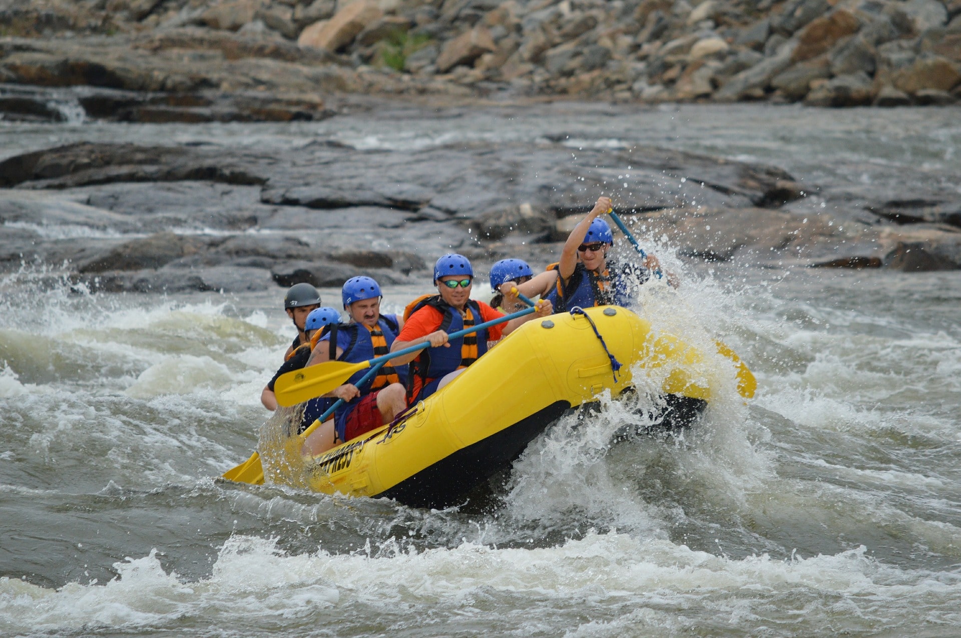 the image shows a group of men in an orange inflatable raft as they battle a rivers whitewater rapids
